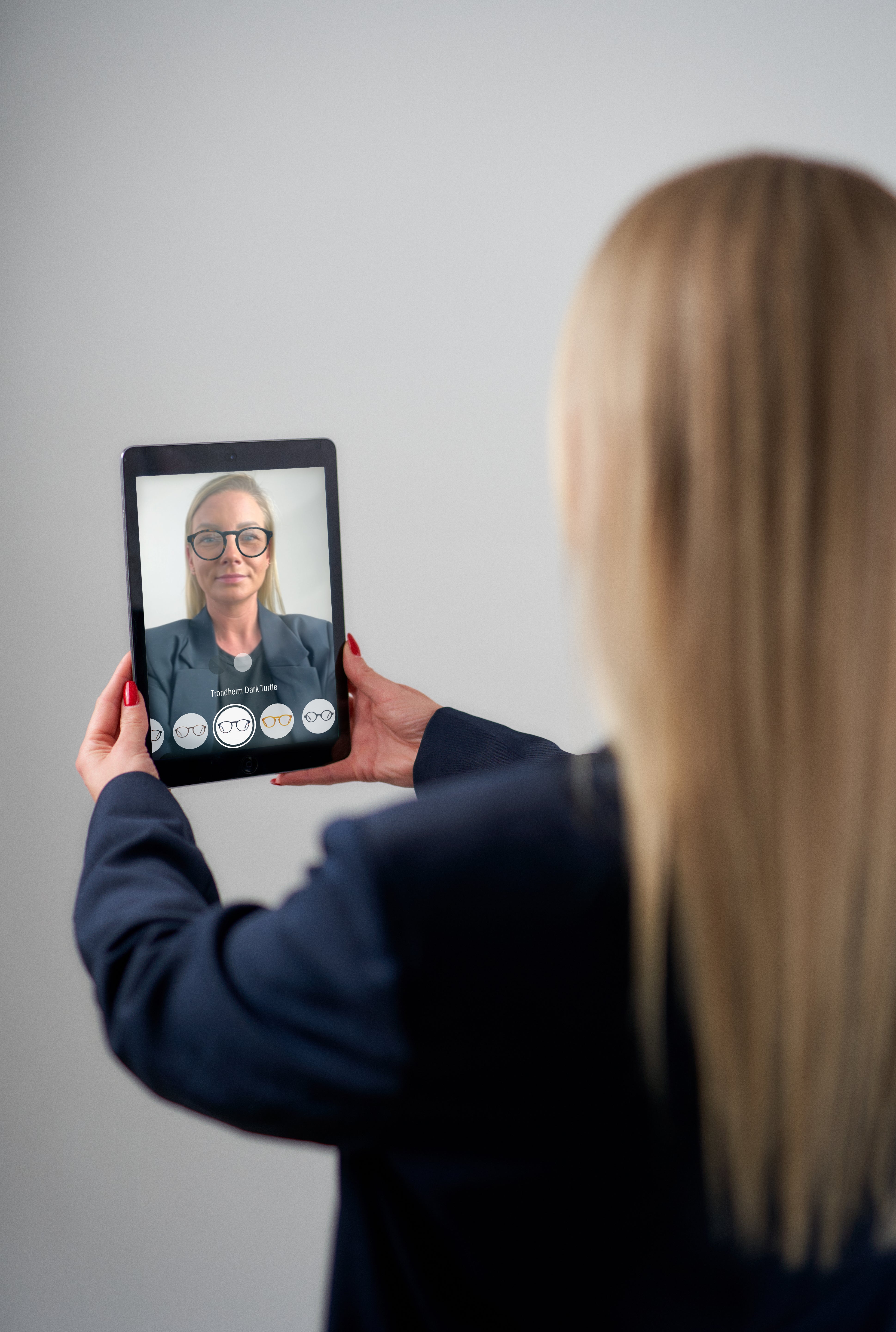 A person holds a tablet showing a virtual try-on of Luxreaders glasses, with options visible on the screen.